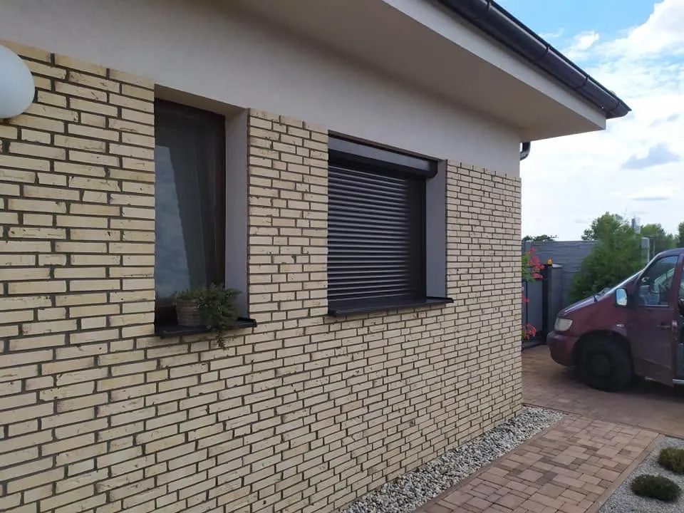 Sötét kültéri redőny egy téglaburkolatú ház ablakán